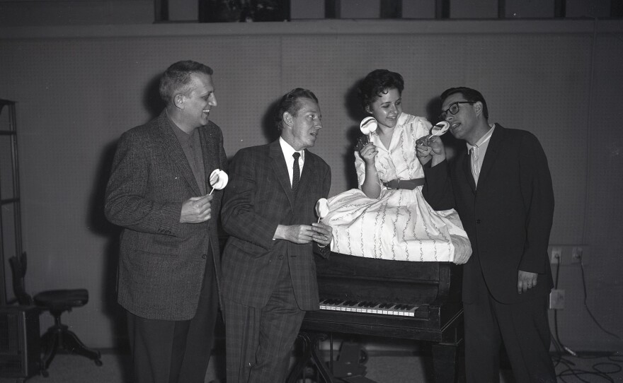 Brenda eating a pop sitting on a piano with Owen Bradley, Dub Allbritten and an unidentified man. (undated photo)