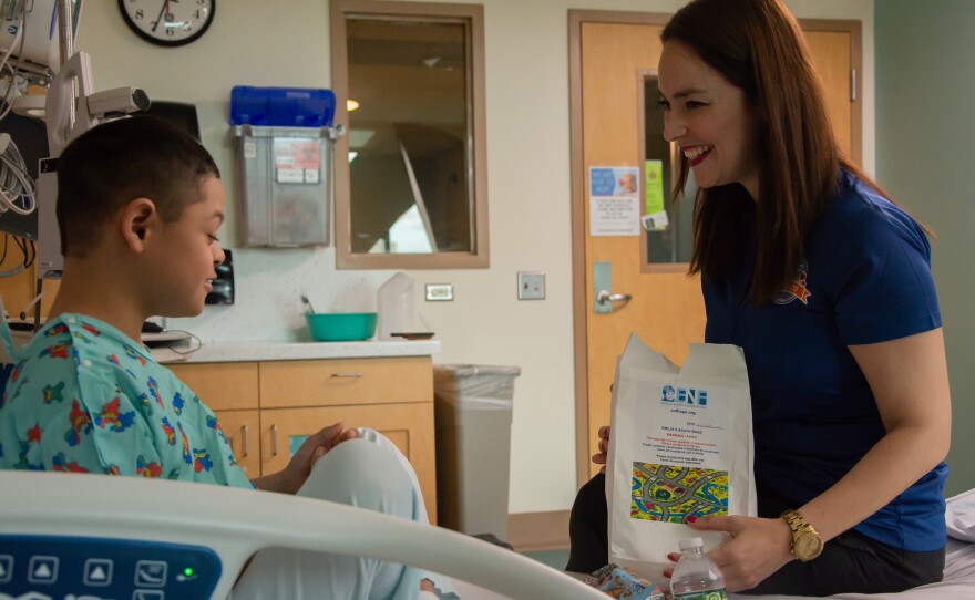 Elsa Morales-Roth (right), executive director of the Emilio Nares Foundation, hands a snack bag to a child recovering from chemoin this undated photo. 