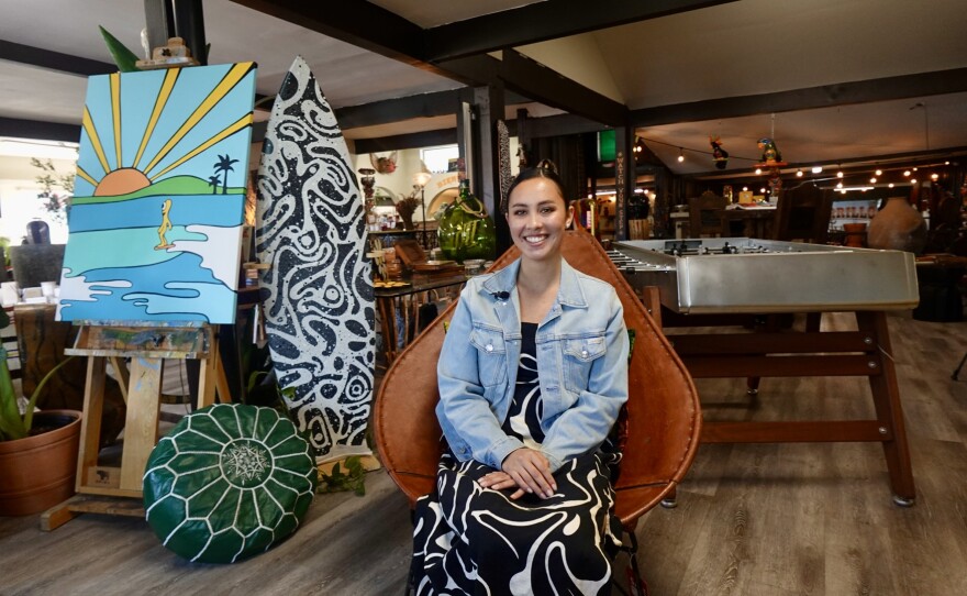 Bella Bowman sitting next to a surfboard she painted(right) as well as her painting titled, 'Bob the blob'(left) inside Carillo Pottery on Jan. 26th, 2026.