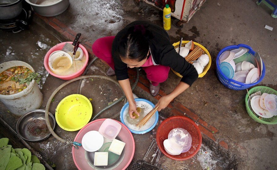 A woman washes dishes on the street in Hanoi, Vietnam. The World Health Organization says the burden of foodborne disease in Southeast Asia is one of the highest in the world.