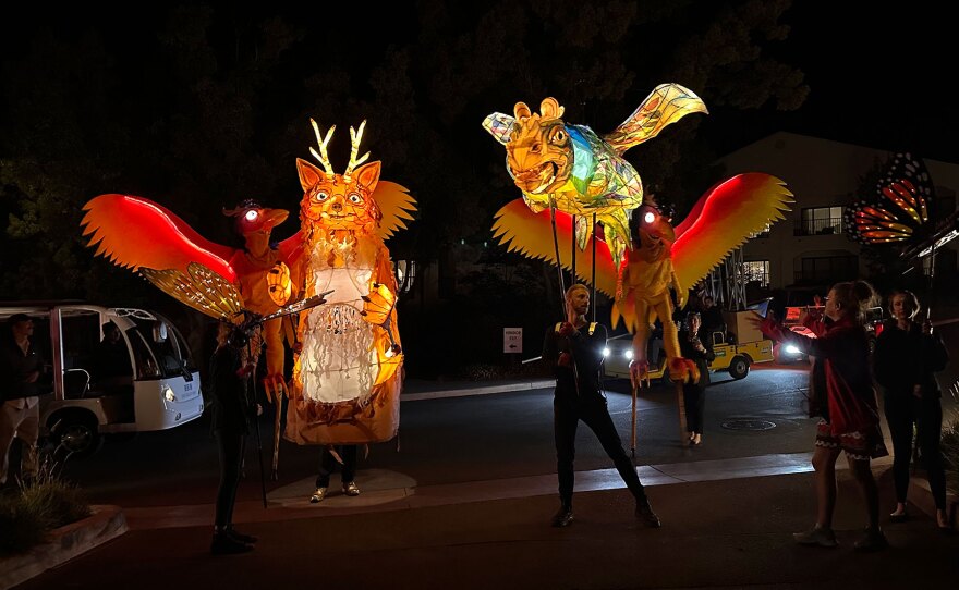 Performers and puppets from Animal Cracker Conspiracy. Several giant animal puppets are shown in the dark, but the puppets are lit from within. The animals are mystical creatures.