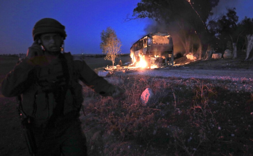 An Israeli soldier stands near a burning bus that was hit by a mortar shell fired from Gaza on Monday.