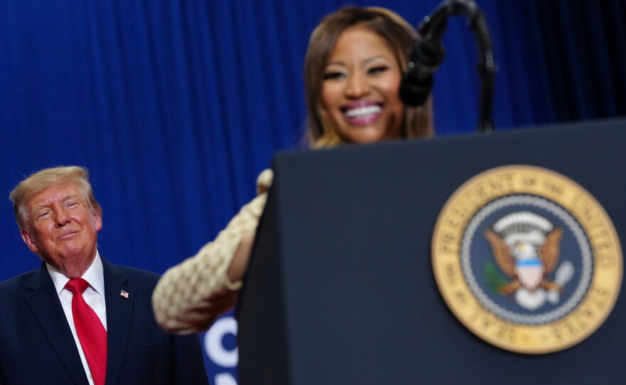 President Donald Trump listens as Nicki Minaj speaks during a campaign rally at McMorran Place Sports and Entertainment Center, Sunday, Oct. 25, 2026, in Port Huron, Mich.