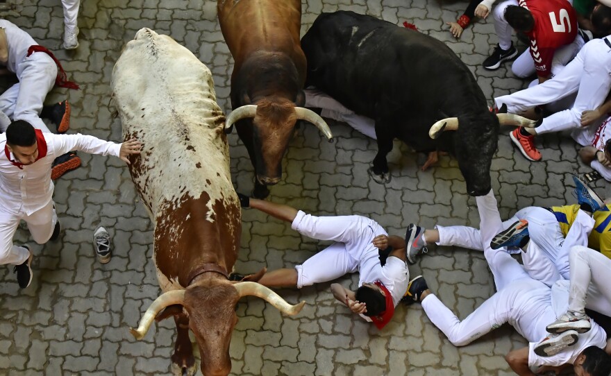 Runners fall during the running of the bulls at the San Fermin Festival in Pamplona, northern Spain, Monday, July 11, 2022.