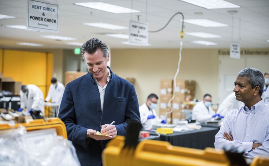 In this March 28, 2020, file photo, Bloom Energy CEO KR Sridhar, right, watches as California Gov. Gavin Newsom writes down a note during a tour with Sridhar of the Bloom Energy Sunnyvale, Calif., campus.