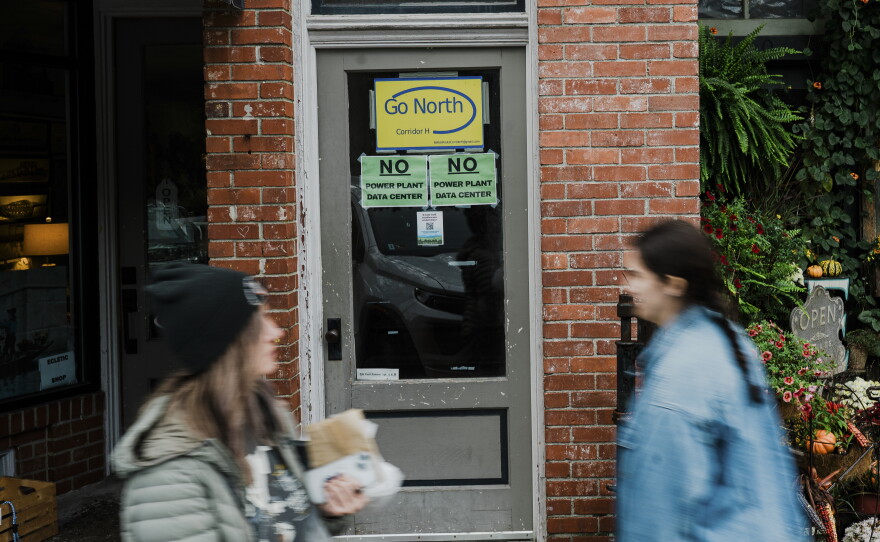 Pedestrians walk past data center protest signs on Front Street in Thomas, W.Va.