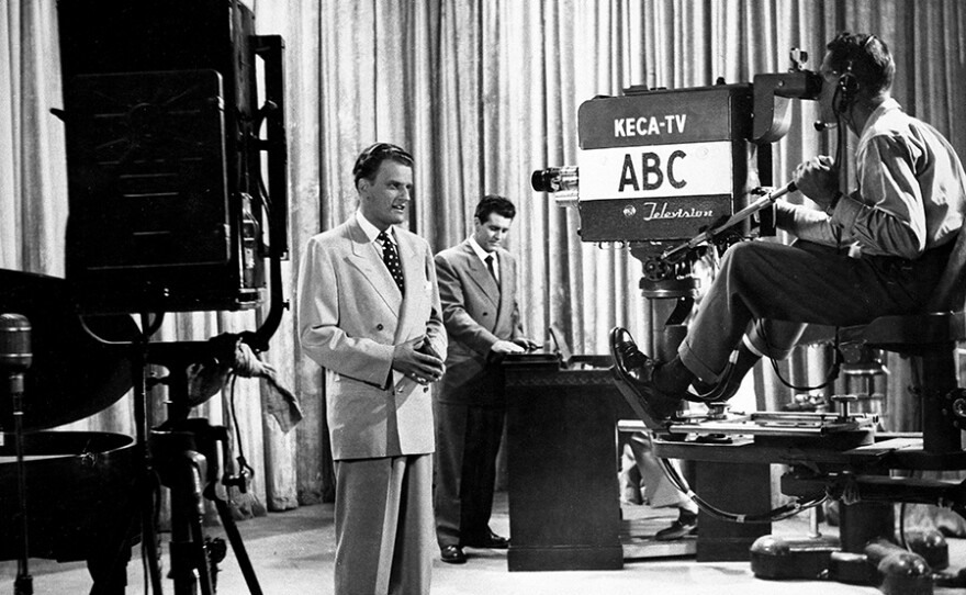 Billy Graham during an early taping of “The Hour of Decision” TV and radio program. Host Cliff Barrows stands at a desk behind him. 1951.