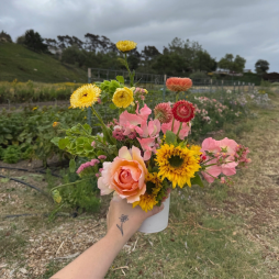 Local Flower Arranging 101 Workshop + Farm Tour - Image of a floral arrangement held up in front of rows of small crops