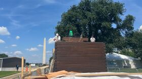 Workers assemble a home resembling an instant log cabin on the National Mall in Washington, D.C., with the Washington Monument behind them.