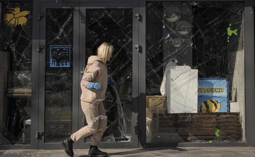A woman removes pieces of broken glass from a shop window after a bombing in Kyiv, Ukraine on March 23.