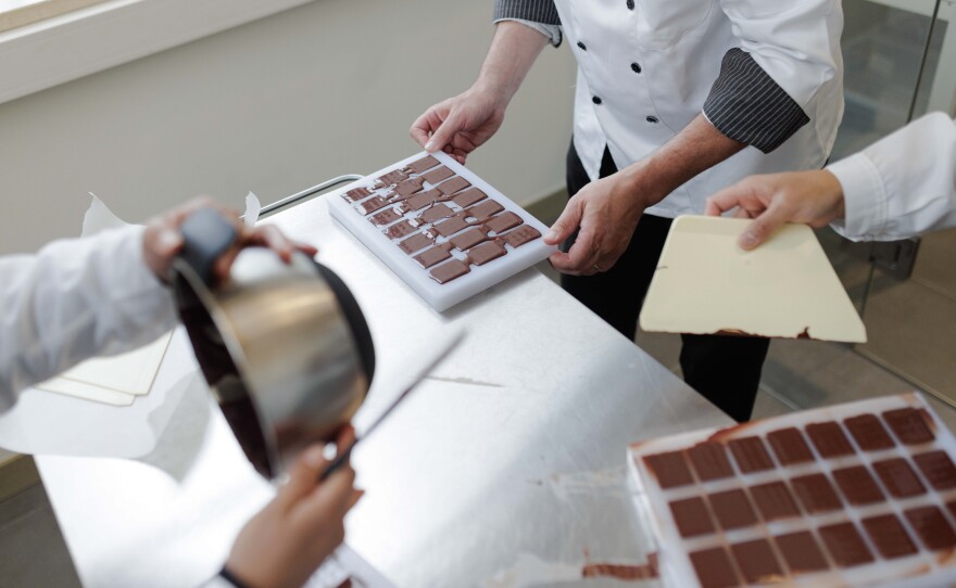 The tempered chocolate is poured into a set of small chocolate molds that are rapped upon the table to remove any air bubbles before chilling.