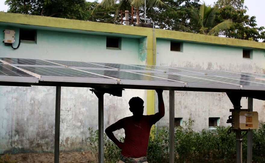 A man stands beneath solar panels that help bring electricity to the village of Rajat Jubilee.