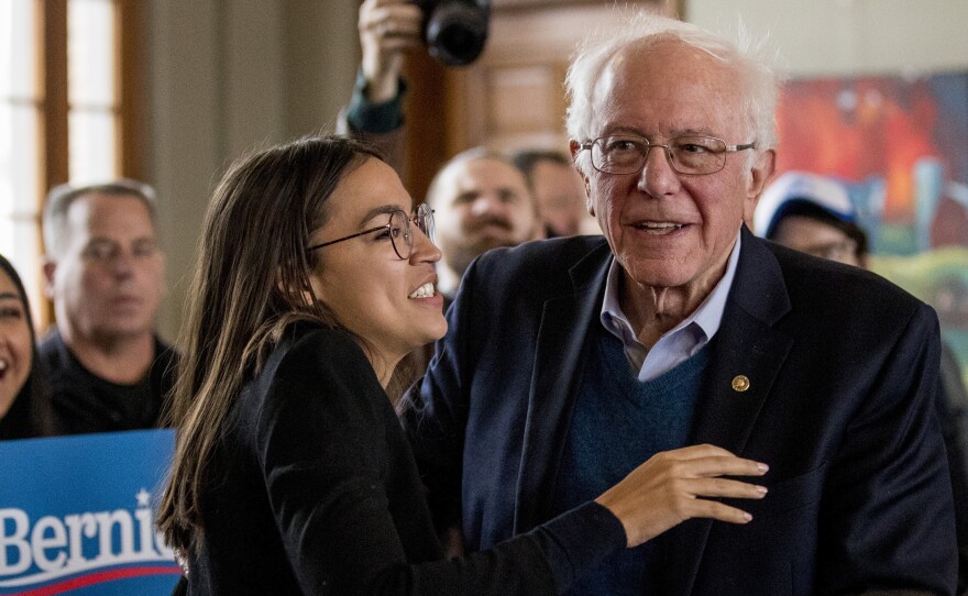 Sen. Bernie Sanders smiles as he is welcomed to the podium by Rep. Alexandria Ocasio-Cortez of New York during a campaign stop in Perry, Iowa.