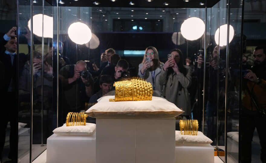 Journalists gather around a glass enclosure with the Dacian gold items, a 2,500-year-old helmet and wristbands, stolen from a museum in the Netherlands and then recovered by Dutch authorities, after they were presented upon being returned at the National Museum of Romanian History, in Bucharest, Romania, Tuesday, April 21, 2026.