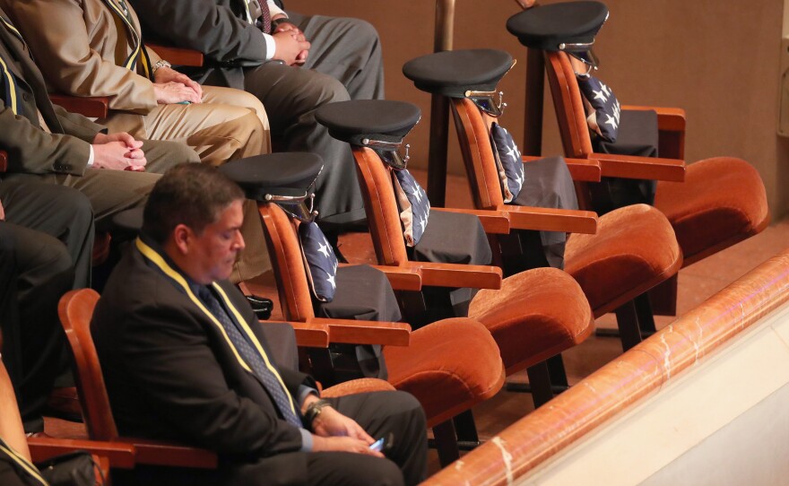 Reserved seats at the memorial service contain American flags and police hats to honor the five slain officers.