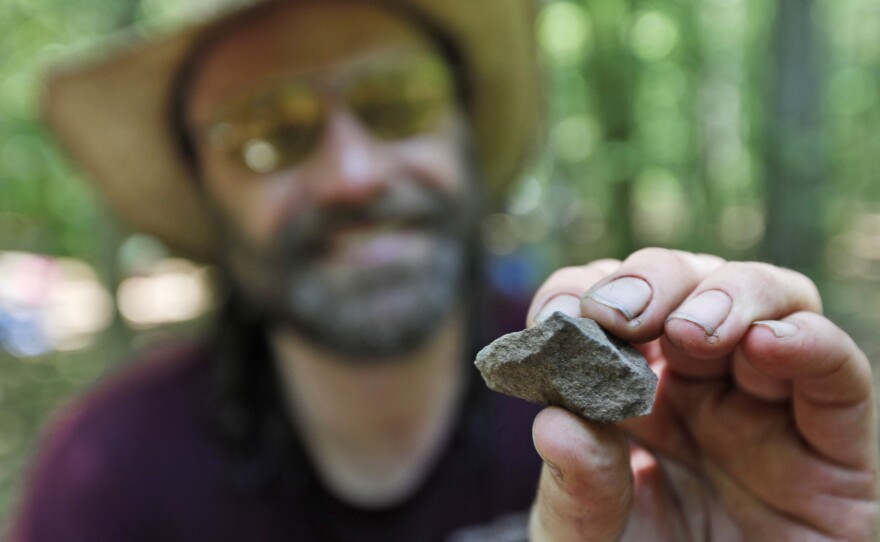 Daniel Sayers has been working for more than a decade in Great Dismal Swamp; here, in 2011, he displays a fire-cracked rock from a dig site. His new book pieces together the stories of those who once lived in settlements scattered on patches of dry land in the swamp.