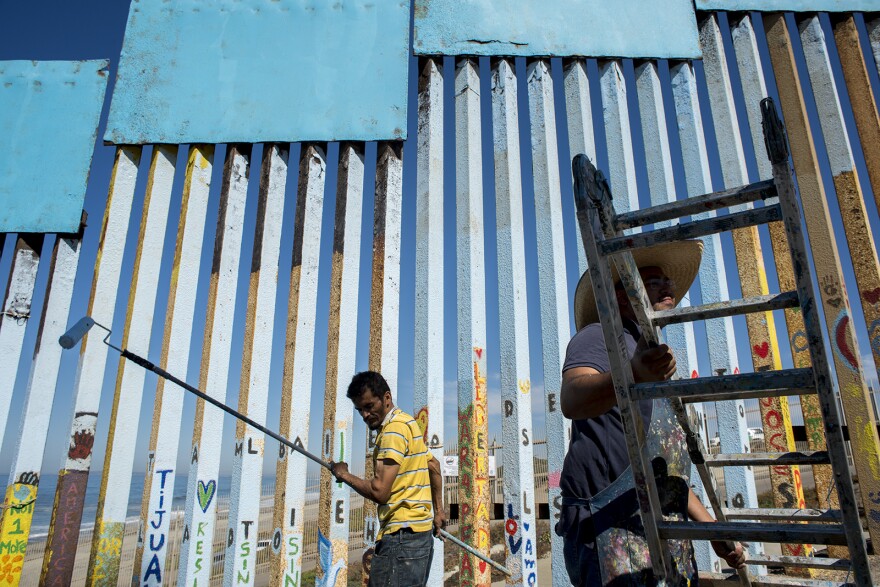 Sergio Tellez, left, volunteers with Enrique Chiu on Oct. 7, 2017, as they paint the easternmost edge of fencing along the U.S.-Mexico border in Tijuana. Tellez used a paint roller to help remove corroded metal from the fencing before adding a new layer of blue.