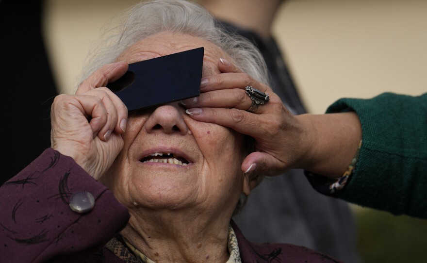 An elderly woman looks through a welding filter during a partial solar eclipse in Bucharest, Romania, Oct. 25, 2022.