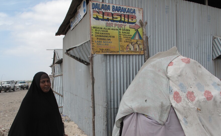 Mrs. Adad Hassan Jimali stands next to a sign for her private camp for displaced persons. The camp, which is in Mogadishu, Somalia, is called Nasiib Camp.