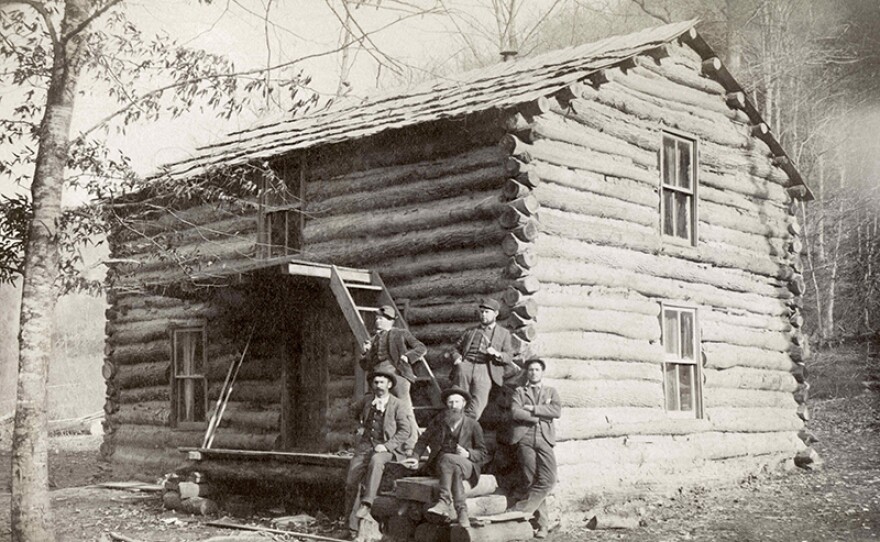 William Anderson Hatfield, center, sits with unidentified associates on the front steps of a two-story log cabin. Circa 1890s.