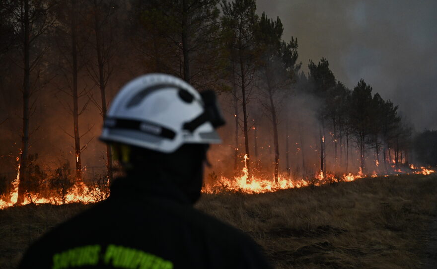 A firefighter walks in front of burning trees as a wildfire rages near Marcheprime, outside, Bordeaux, France, July 26, 2026.