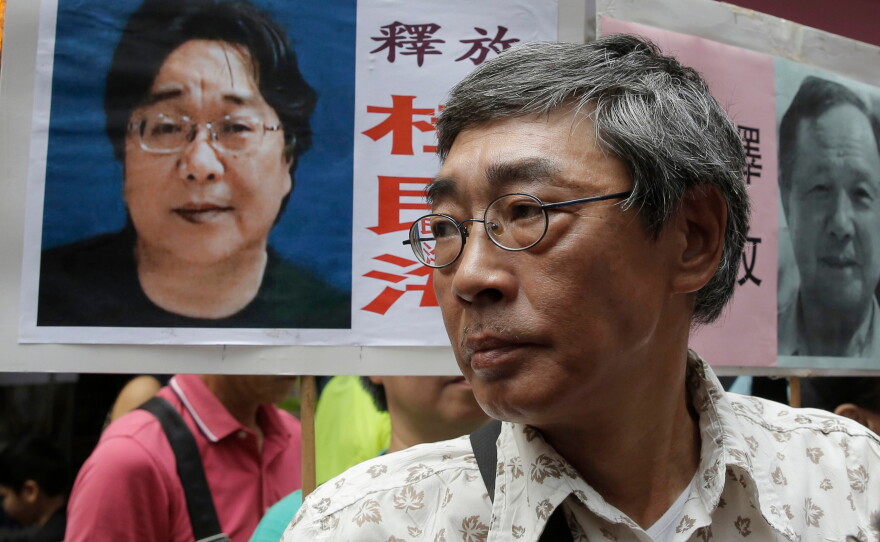 FILE - Freed Hong Kong bookseller Lam Wing-kee stands next to a placard with a picture of missing bookseller Gui Minhai, left, in front of his book store during a march in Hong Kong on June 18, 2016.
