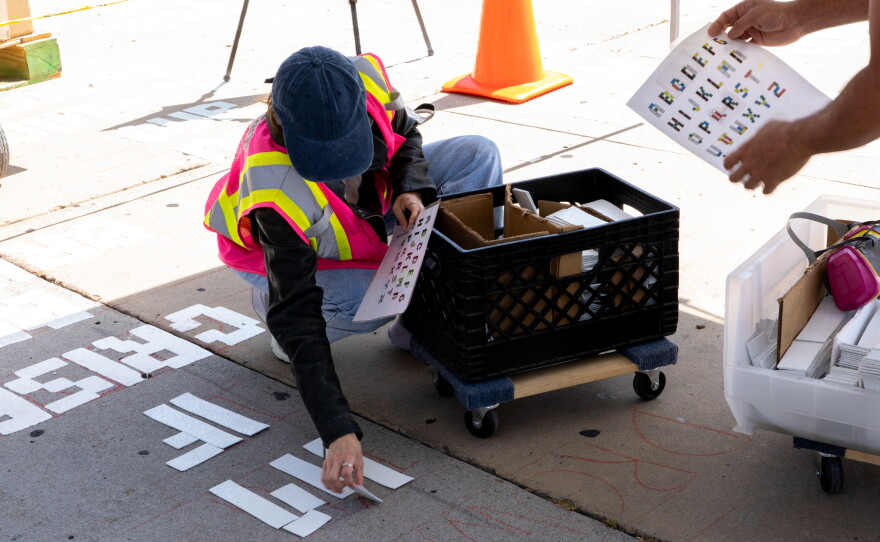 A project worker lays strips of heat-activated road marking material to form the letters of poetry in a City Heights alley on Tuesday, June 18. 2024.