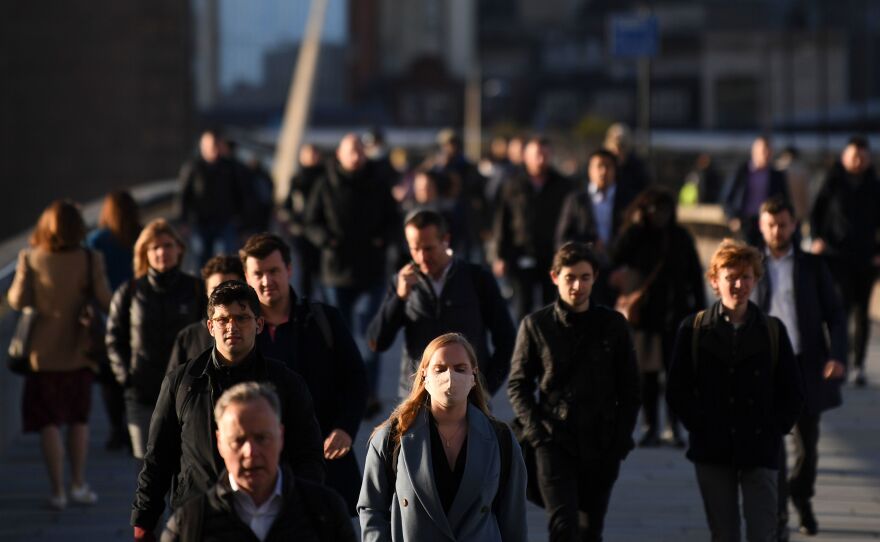 Commuters walk over London Bridge toward the City of London during the morning rush hour on Thursday. The city and other large areas are now under a high alert for the coronavirus, as health officials enact new restrictions.