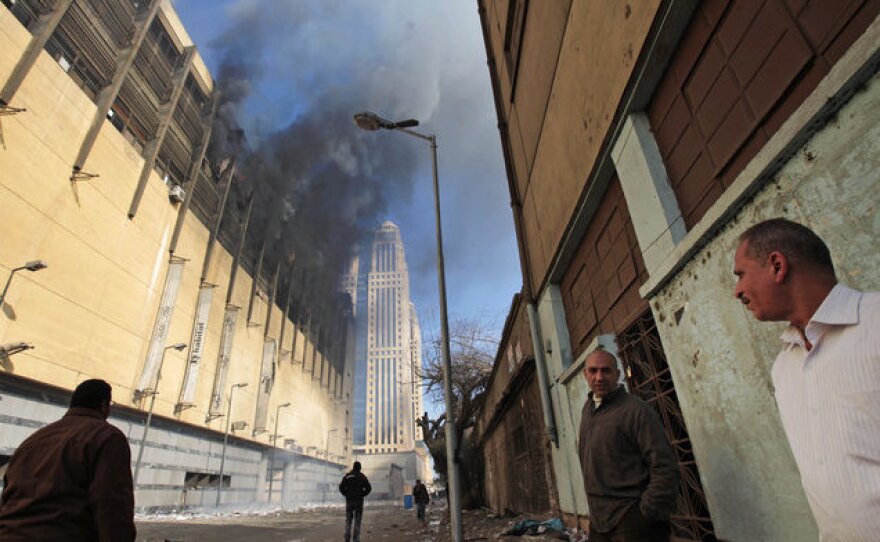 Egyptians watch smoke billow from a shopping center in Cairo on Sunday that was looted, damaged and set on fire overnight.