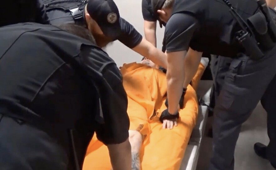 A man is held down by a group of officers at Thomson prison as they try to place him in a four-point restraint.
