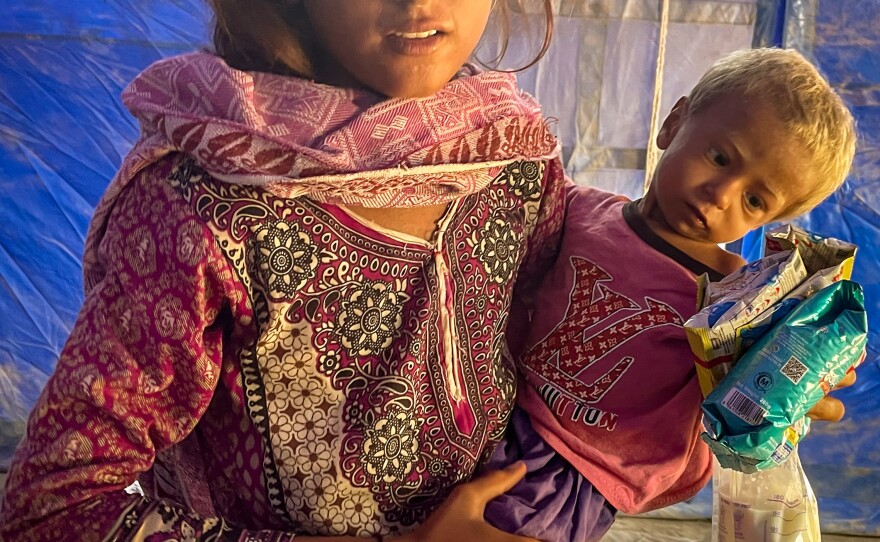 A young girl named Ruksana holds her baby brother, Zaman, and food supplements that Mankani has given her. Ruksana explains that their mother is worried because she doesn't have enough food to give them.