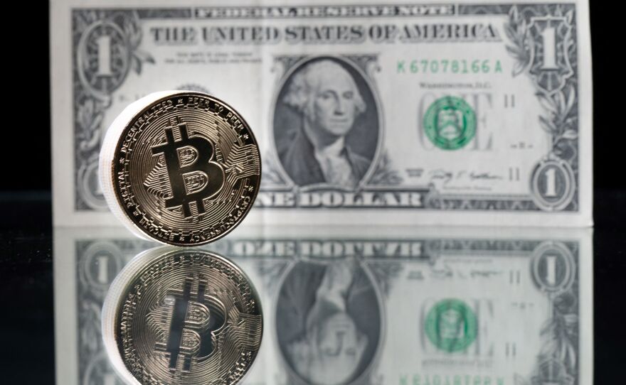 This photograph taken on April 26 in Paris shows a physical imitation of the Bitcoin cryptocurrency pictured with a one-dollar bank note. Cryptocurrencies like Bitcoin are plunging over a range of factors, including the spillover impact from falling stock markets and fears about increased regulations.