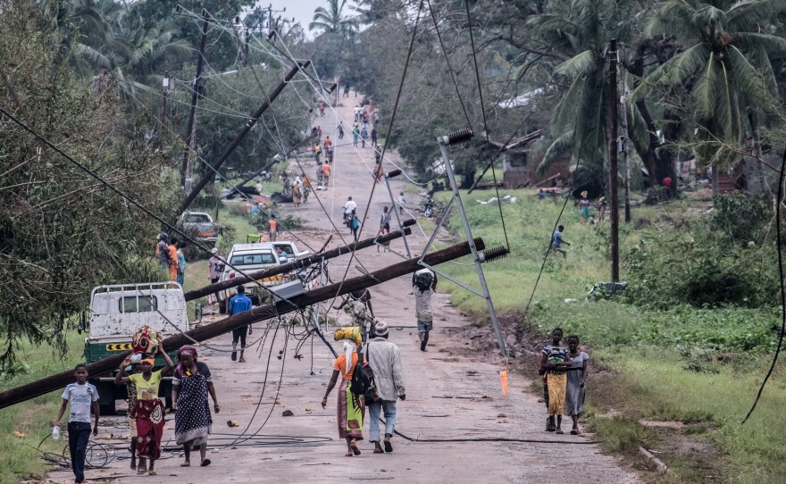 People walk along a main road in Macomia past power lines downed by Cyclone Kenneth. Vehicles could just about get through by driving on the side of the road.