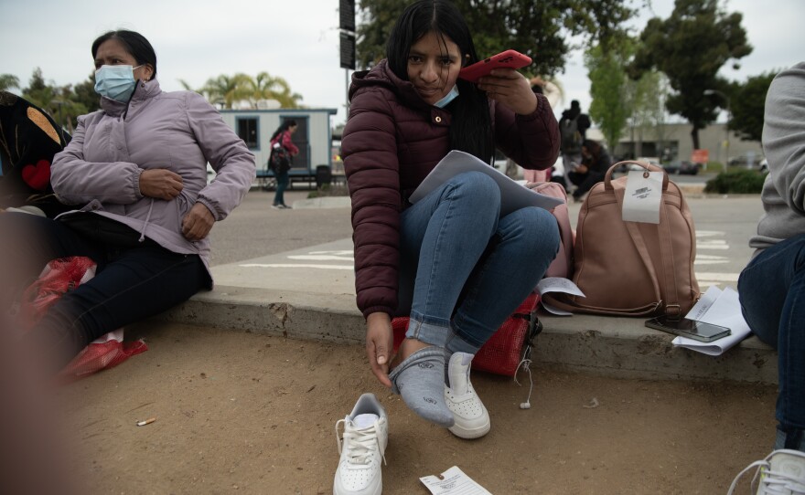 A South American migrant struggles to redo her shoelaces while also calling her family in San Ysidro, April 19, 2024. Migrants detained by CBP have to remove their shoelaces while in custody. 