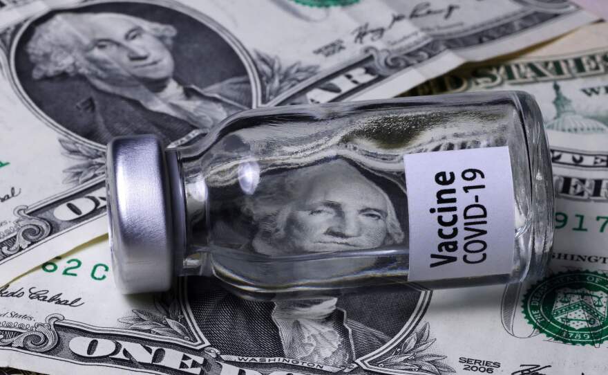 A COVID-19 vaccine vial sits on top of dollar bills.