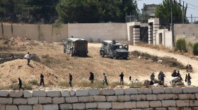 Israeli soldiers stand guard next to settlers in front of Palestinian homes that they have blockaded in the village of Qusra, south of Nablus, in the occupied West Bank, Wednesday, Aug. 12, 2026.