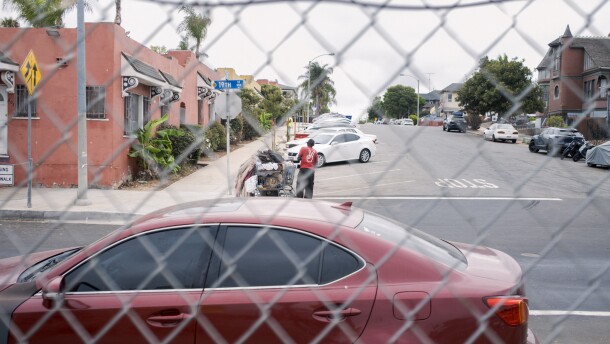 A man transports his belongings in a shopping cart on the city's side of a chain link fence in San Diego on Friday, Aug. 15, 2025.