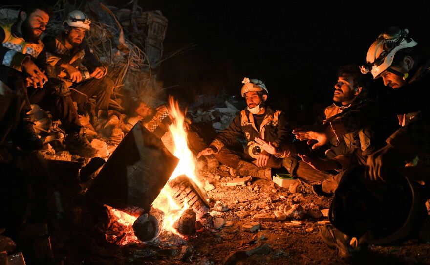 Members of the Syrian civil defense, known as the White Helmets, warm themselves by a fire next to the rubble of a collapsed building late on Tuesday in Jandairis, as search and rescue operations continue following a deadly earthquake.