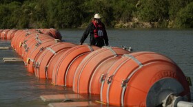 A kayaker walks past large buoys being used as a floating border barrier on the Rio Grande, Aug. 1, 2023, in Eagle Pass, Texas.