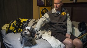Jon Miller sits in his bedroom with his dog, Carlos, whom he received as a present for successfully completing cancer treatment a decade ago. Miller sustained severe brain damage, and requires the help of home health aides to continue living in his home.