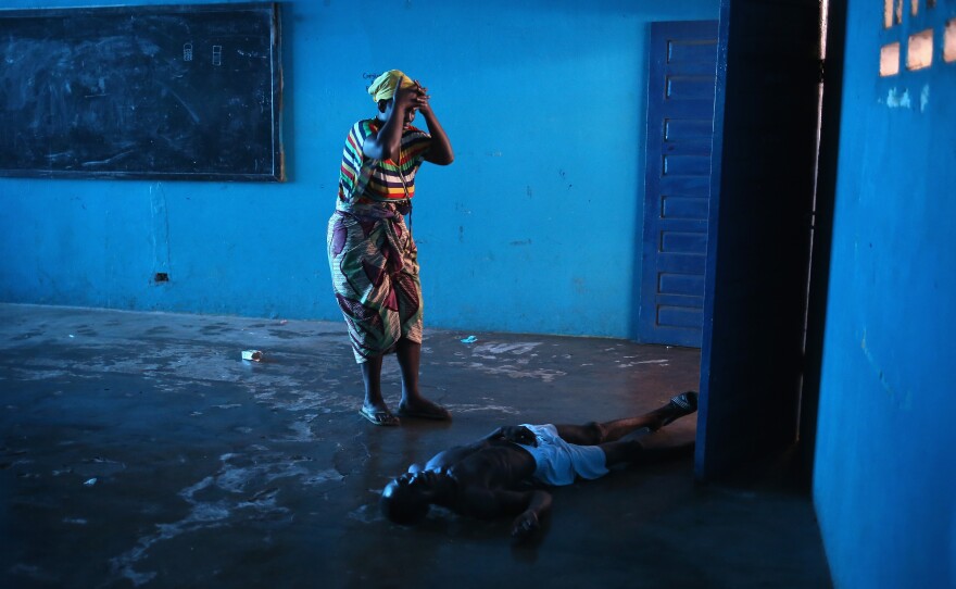 Umu Fambulle stands over her husband, Ibrahim, who'd fallen and knocked himself unconscious in an Ebola ward in Monrovia, Liberia.