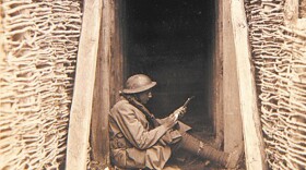 U.S. artilleryman sits on the ground writing, World War I; March 7, 1918
