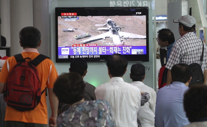 People watch a news program reporting on the accident at Seoul Railway Station in South Korea. The writing on the screen reads, "Fire on the ceiling of the airplane."