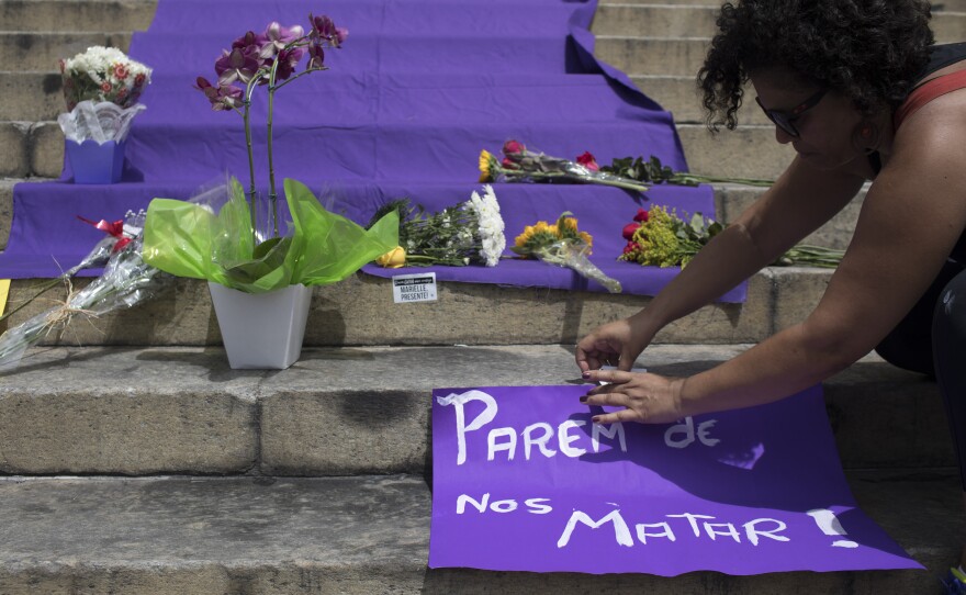 A woman positions a sign with a message that reads in Portuguese: "Stop Killing Us!" on the steps of City Hall where people gathered to pay their respects to slain council member Marielle Franco and her driver.