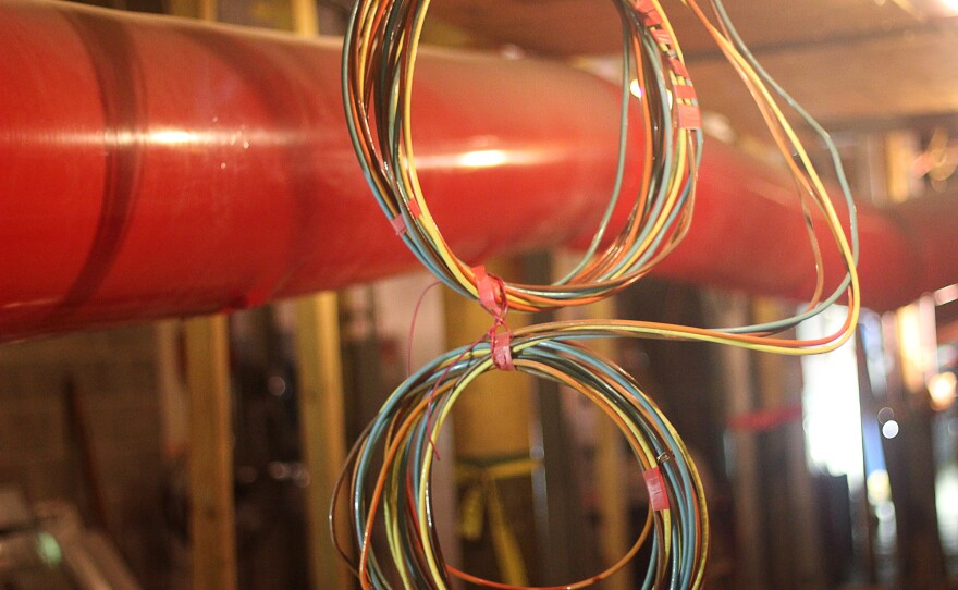 Electrical switching equipment has been moved out of this basement space to a ground floor area that used to hold an eyeglass shop. The large orange pipe is made of plastic sheeting, and air flows through to dehumidify the basement.