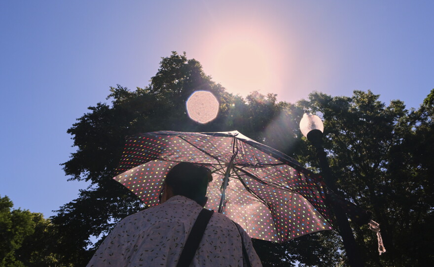 With temperatures hovering near 100 degrees, a woman protects herself from the sun while walking through Boston Common in 2025.