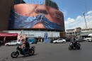 Vehicles drive past a billboard with graphic showing Strait of Hormuz and sewn lips of U.S. President Donald Trump in a square in downtown Tehran, Iran, Saturday, May 2, 2026.