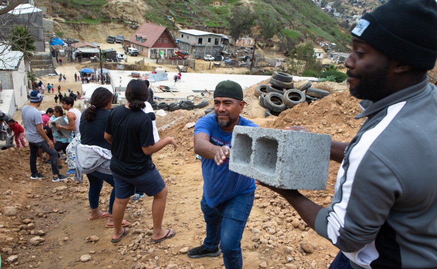 Dozens of people work to move a truckload of cinder blocks for new construction at the Templo de Embajadores shelter in Tijuana, Dec. 1, 2022.
