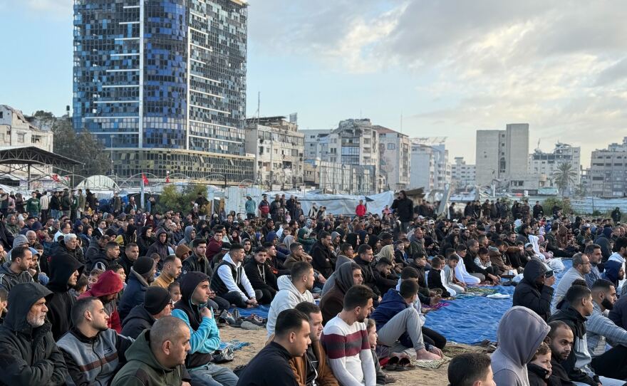 People listen to sermons outside, near destroyed and damaged buildings.