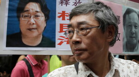 FILE - Freed Hong Kong bookseller Lam Wing-kee stands next to a placard with a picture of missing bookseller Gui Minhai, left, in front of his book store during a march in Hong Kong on June 18, 2016.